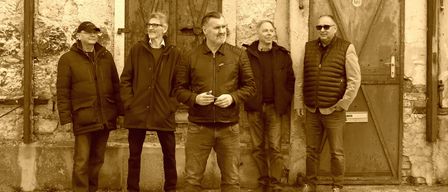 Five men stand in front of a building with old wooden doors. They are dressed in winter clothes. They are smiling and seem to be posing for a photo.