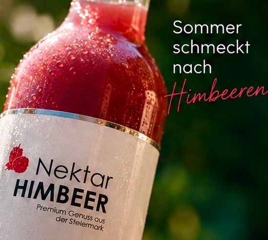 Ein Nahaufnahme einer Flasche Nektar Himbeeren, ein roter beerengeschmackvoller Getränk, mit Wassertropfen auf der Oberfläche und einem grünen Hintergrund.