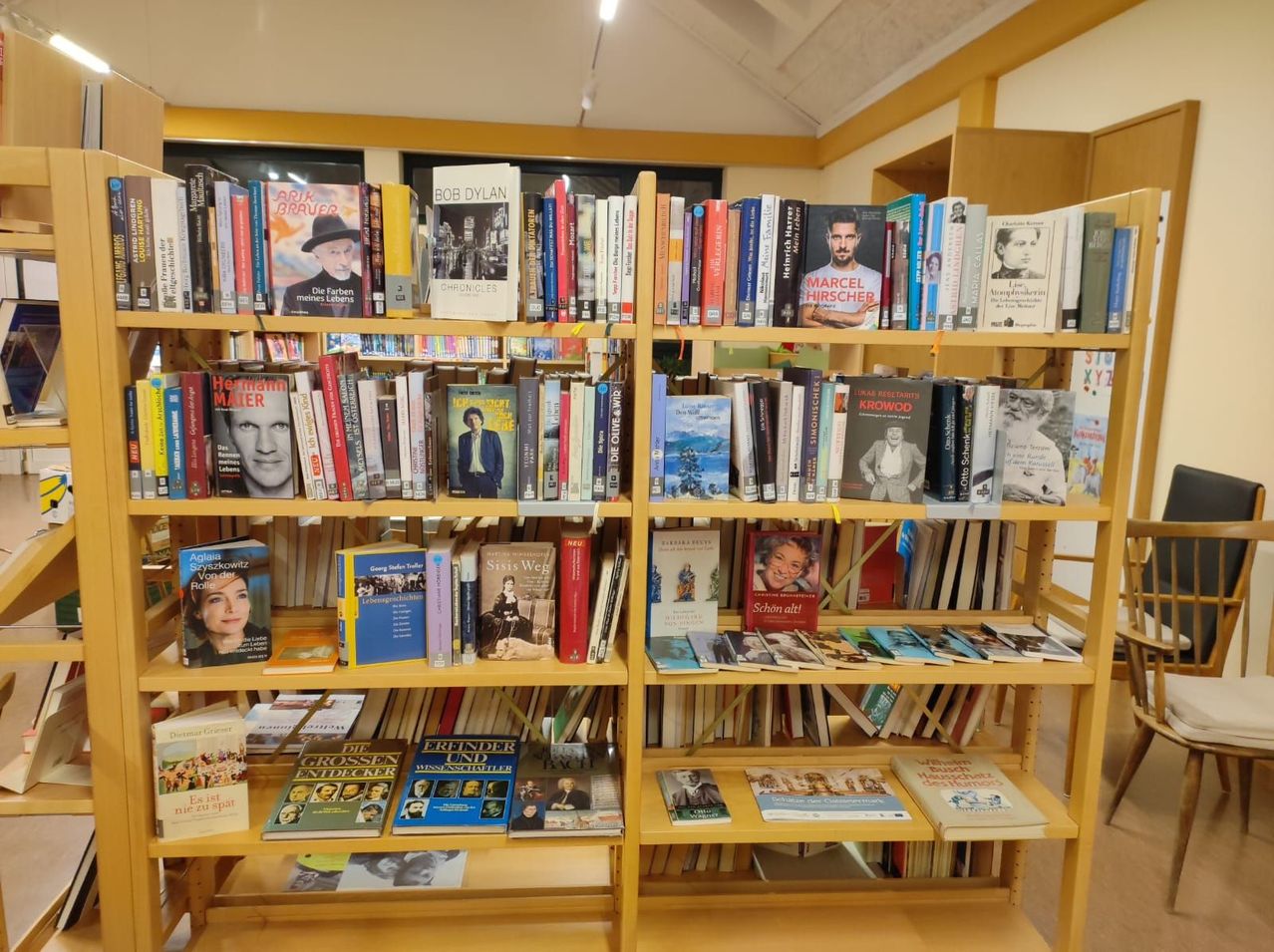 Zwei hölzerne Bücherregale gefüllt mit Büchern, einige mit Cover-Kunst von Menschen, stehen in einem Raum. Eine Deckenleuchte ist oben im Raum.