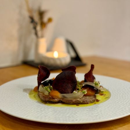 Ein Gericht mit Fleisch und Gemüse auf einem weißen Teller, beleuchtet von einer Kerze auf einem Tisch.