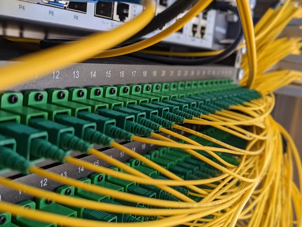 Eine Nahaufnahme eines Serverraums mit zahlreichen gelben und grünen Ethernet-Kabeln, die an Anschlüssen eines grauen Serverpanels angeschlossen sind.
