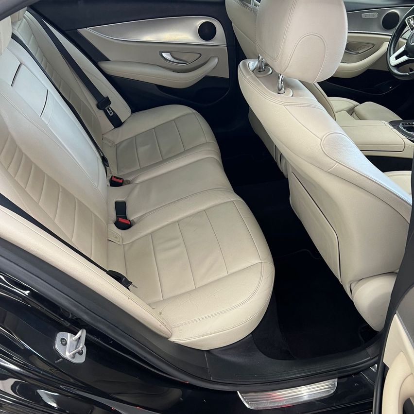 Der Innenraum eines Luxusautos wird gezeigt und zeigt beige Ledersitze, einen Sicherheitsgurt und ein Lenkrad. Die Autotür ist geöffnet und zeigt die Details des Innenraums.