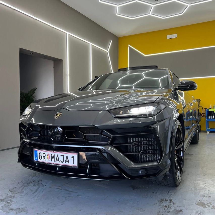Ein schwarzer Lamborghini Urus SUV mit dem Kennzeichen GR-MAJA 1 steht in einer Garage mit gelben Wänden und Sechseckbeleuchtung.