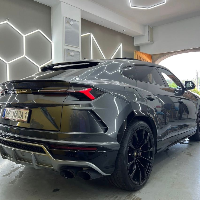 Ein Lamborghini Urus SUV steht in einer Garage mit modernem Innendesign, das hexagonale Lichter an der Wand aufweist.