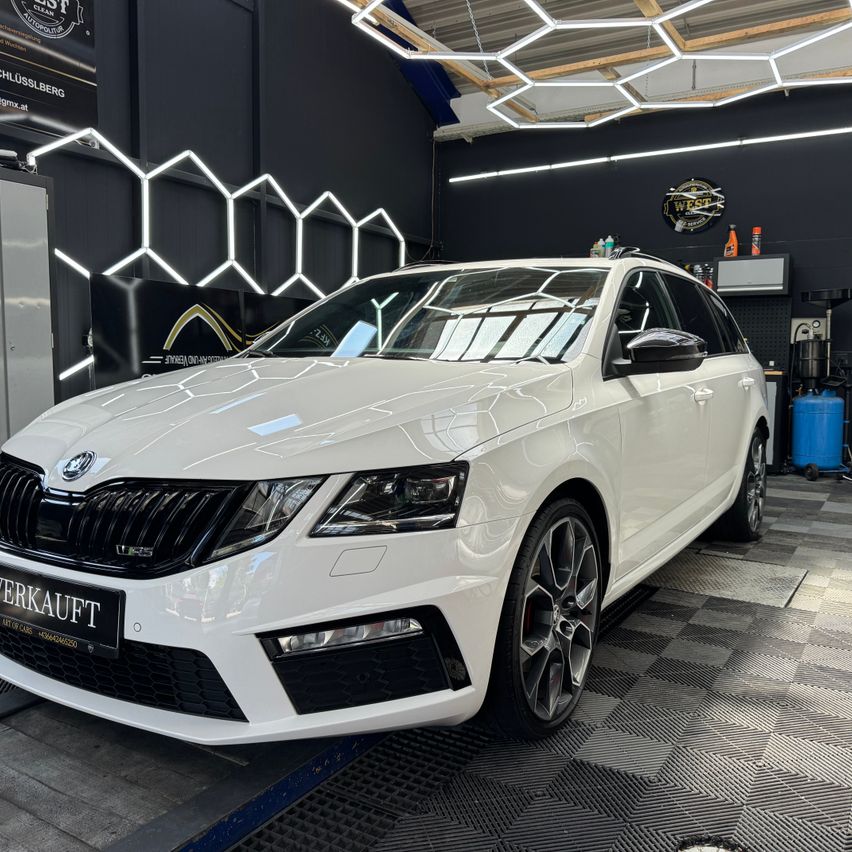 A white Skoda Octavia RS is parked in a garage with a checkered floor, illuminated by ceiling lights. The car has a glossy finish and a license plate that reads 'VERKAUFT'.