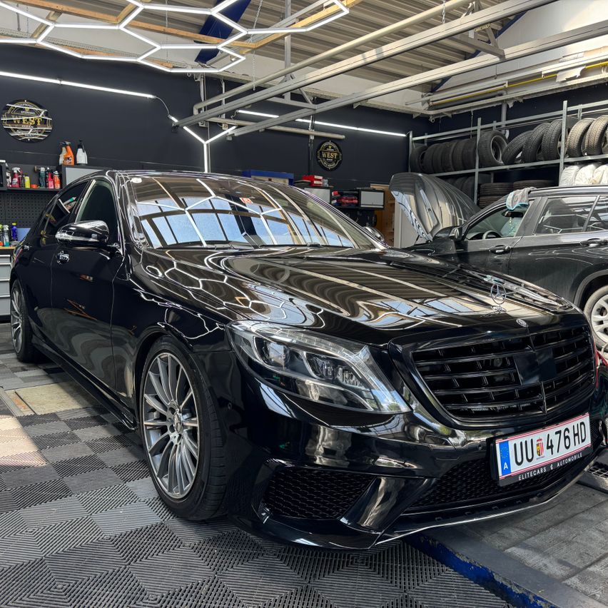 A black Mercedes-Benz S63 AMG is parked in a garage with a hood lifted, showcasing its sleek design and chrome accents.