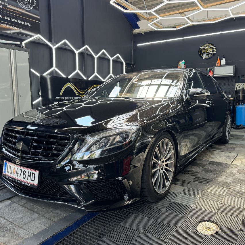 A black Mercedes-Benz S63 AMG is parked on a lift in a car wash with a clean and shiny appearance.