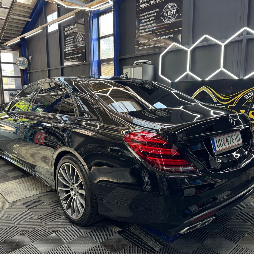 A black Mercedes-Benz S-Class is parked in a car shop with a clean, glossy finish and illuminated red taillights.