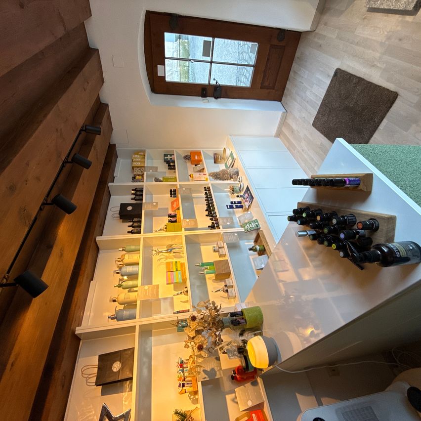 Eine Draufsicht auf einen Boutique-Laden mit Holzregalen voller verschiedener Produkte, einer Lampe und einem kleinen Strauß. Der Laden hat Holzböden und Wände.