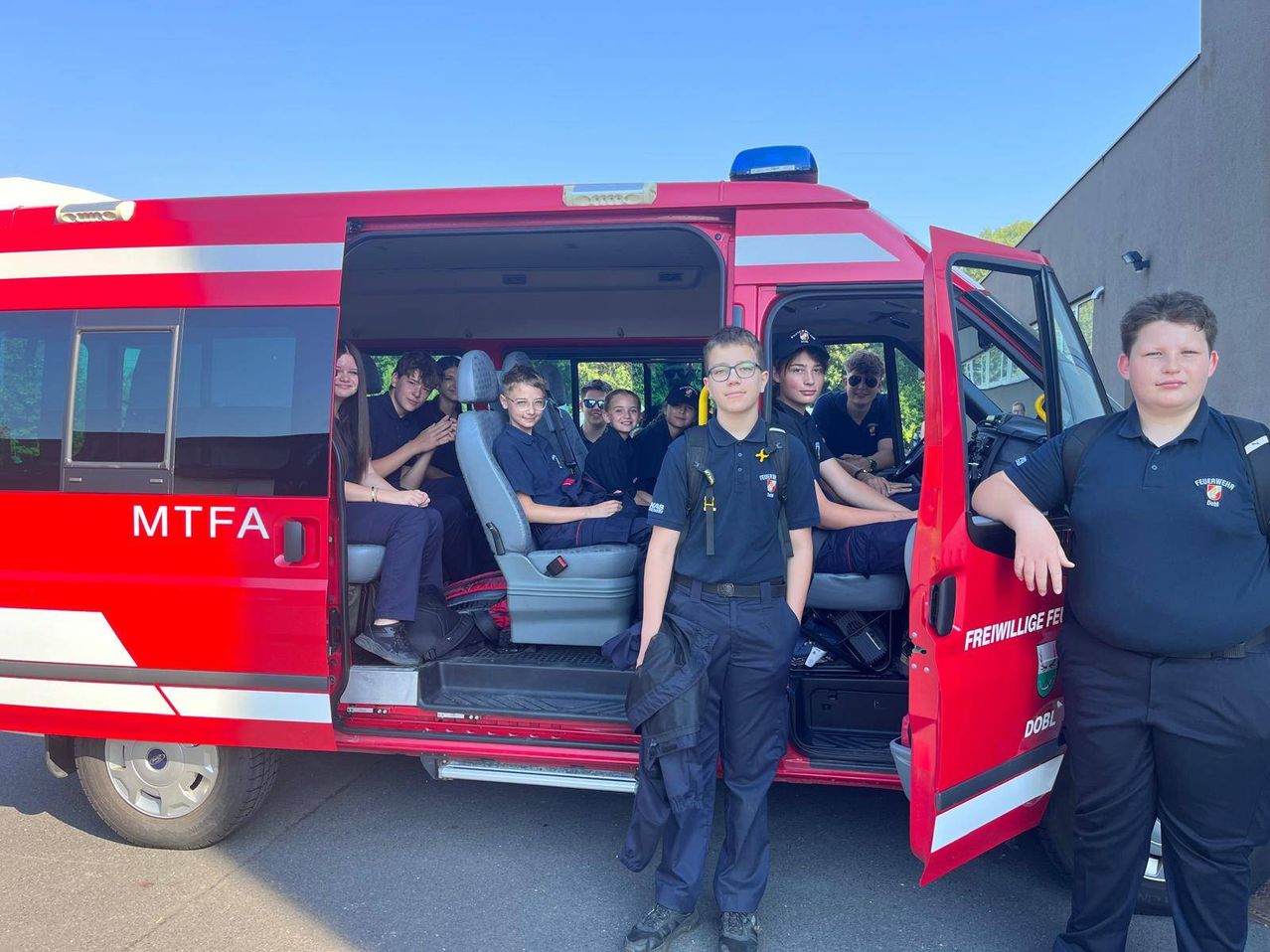 Eine Gruppe von Schülern sitzt in einem roten Feuerwehrauto, während ein Schüler draußen steht. Die Tür des Autos ist geöffnet und zeigt das Innere.