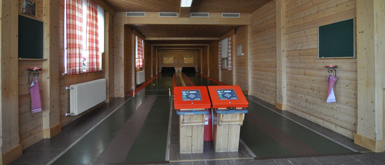 Eine leere Bowlingbahn mit Holzwänden und -böden, zwei rote Maschinen am Ende.