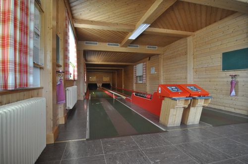 Eine leere Bowlingbahn mit Holzwänden und -böden, mit einer roten Bowlingbahn und zwei orangefarbenen Ballrückgabemaschinen.