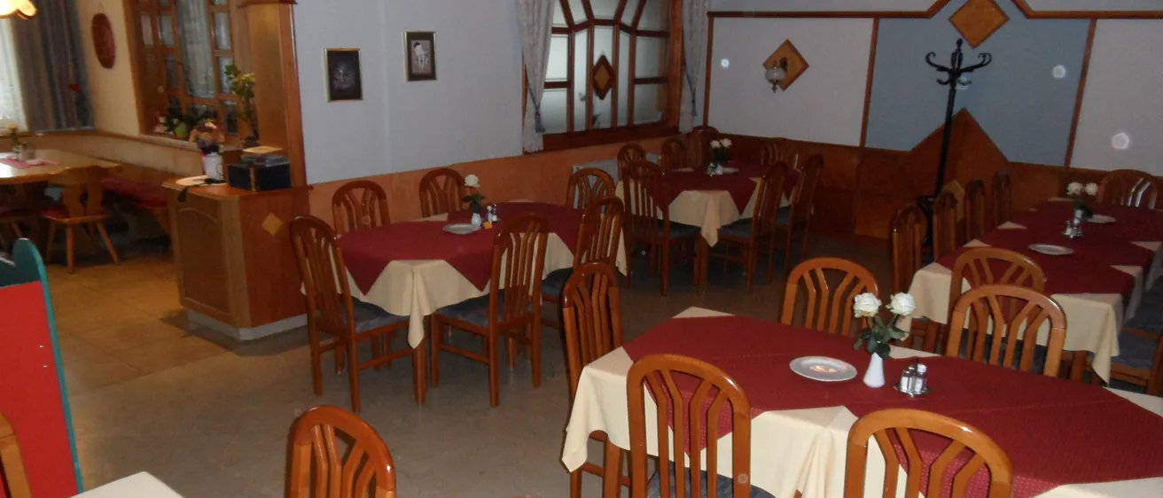 Ein leeres Restaurant mit geordneten Tischen und Stühlen, jeder Tisch hat eine rot-weiße Tischdecke und einige Tische haben Blumen in weißen Vasen.