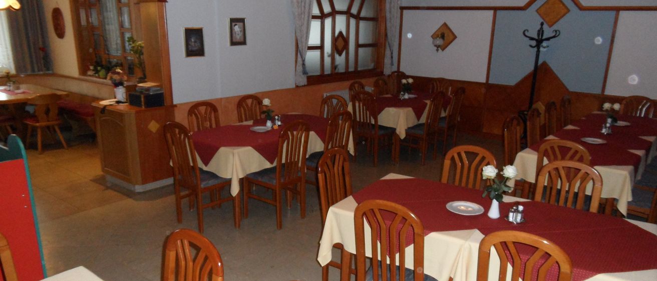 Ein leeres Restaurant mit geordneten Tischen und Stühlen, jeder Tisch hat eine rot-weiße Tischdecke und einige Tische haben Blumen in weißen Vasen.