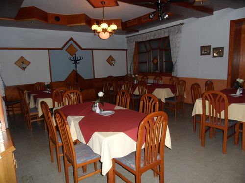 Ein Restaurant-Essbereich mit Holzstühlen und -tischen, einer Kronleuchter und einem Fenster mit Vorhängen.