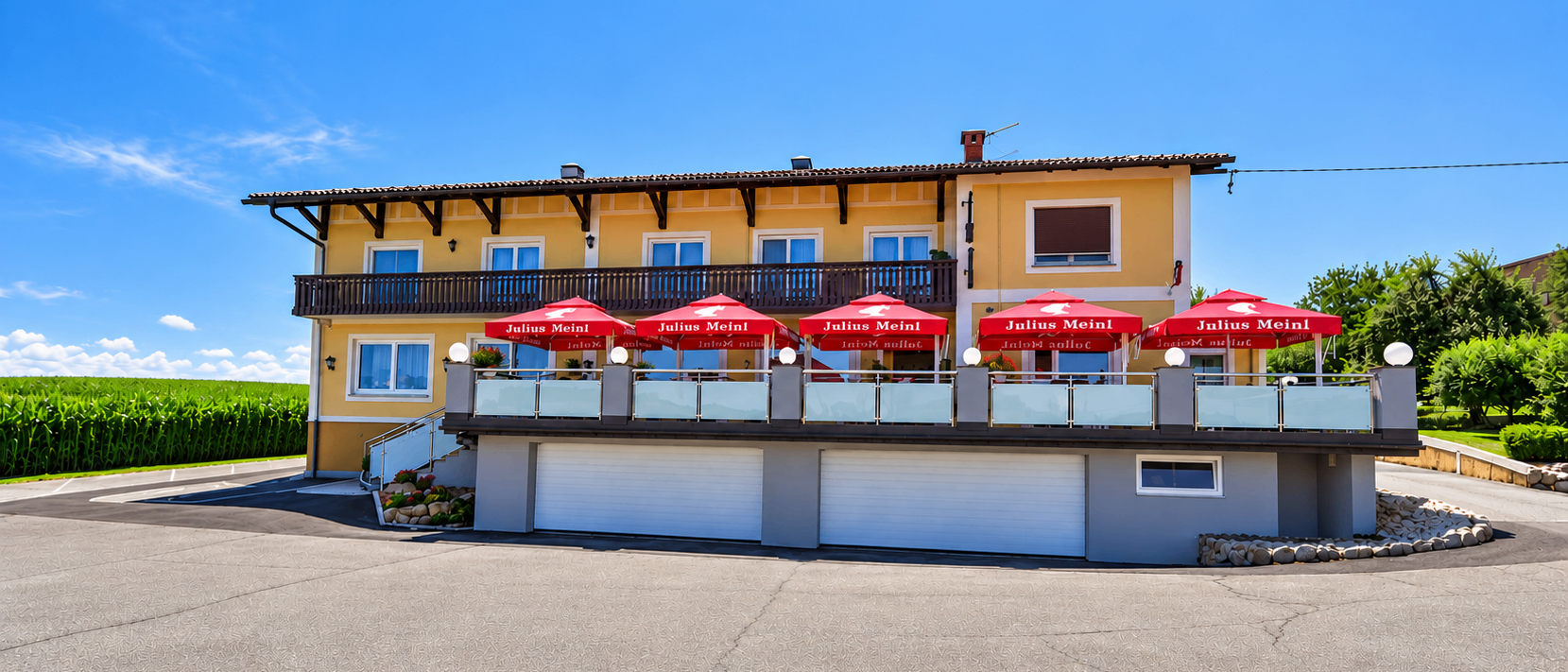 Ein gelbes Gebäude mit mehreren Fenstern und roten Sonnenschirmen auf dem Balkon. Der Name Julius Meinl steht auf den Schirmen.