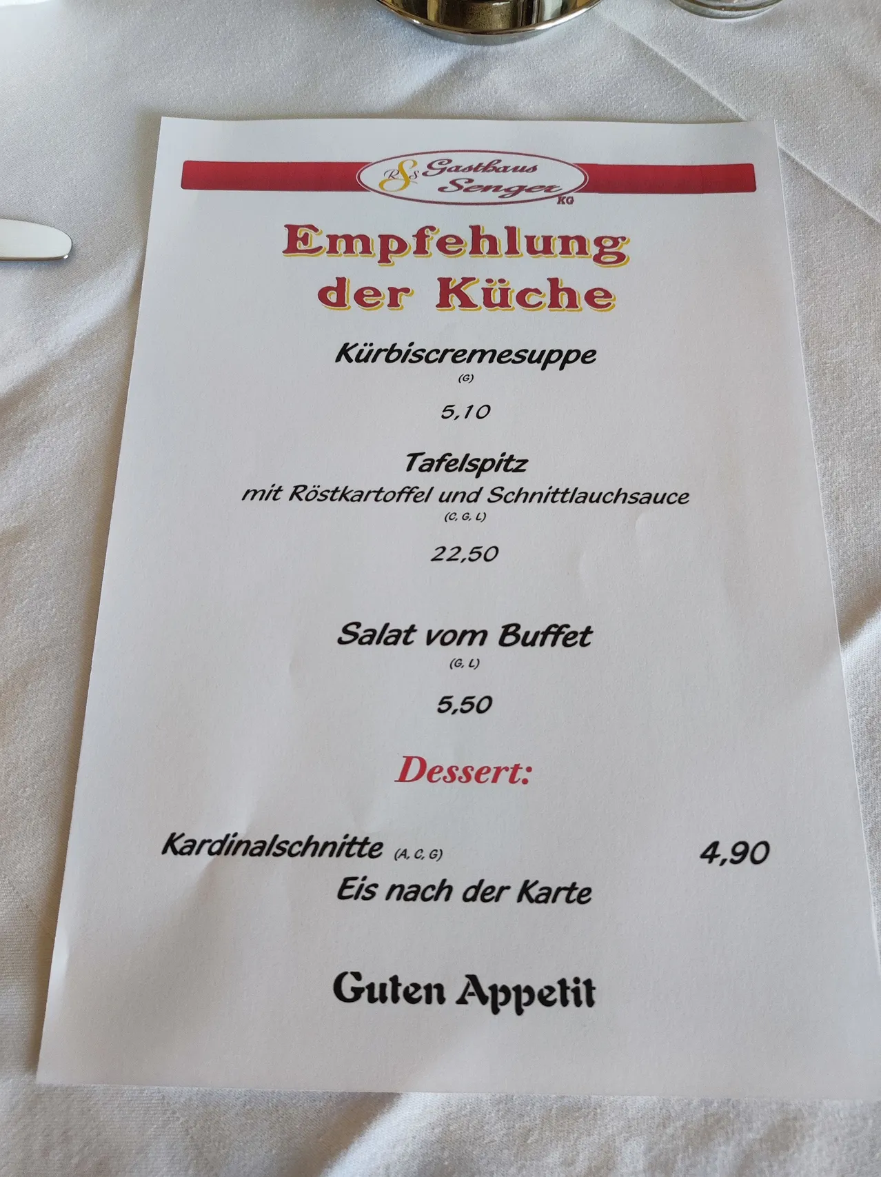 Ein Menü mit rotem Rand, das Gerichte wie Kürbiscremesuppe, Kartoffelsalat und ein Dessert namens Kardinalschnitte mit Eiscreme-Optionen bietet. Die Preise sind in Euro angegeben.