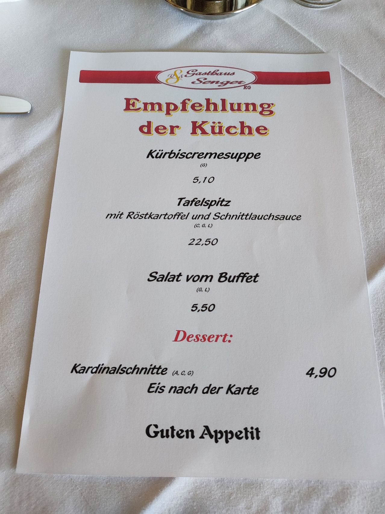 Ein Menü mit rotem Rand, das Gerichte wie Kürbiscremesuppe, Kartoffelsalat und ein Dessert namens Kardinalschnitte mit Eiscreme-Optionen bietet. Die Preise sind in Euro angegeben.