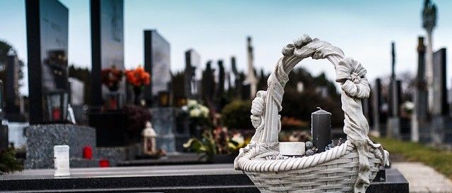 Ein Friedhof mit mehreren Grabsteinen, einem Korb mit einer Kerze und Blumen auf einem Granitgrab und anderen dekorativen Gegenständen.