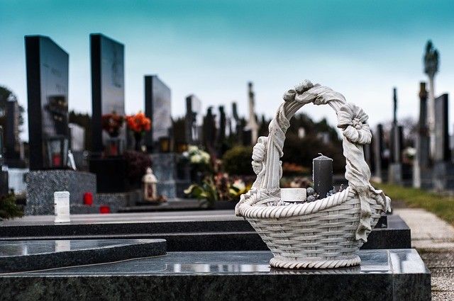 Ein Friedhof mit Grabsteinen, einem Korb mit Kerzen und einer kleinen Vase mit Blumen.