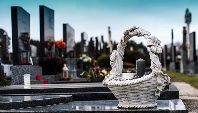 Ein Friedhof mit Grabsteinen, einem Korb mit Kerzen und einer kleinen Vase mit Blumen.