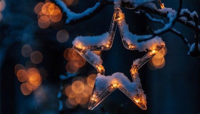Ein sternförmiges Ornament mit Lichtern hängt an einem verschneiten Ast, beleuchtet vor einem dunklen Hintergrund.