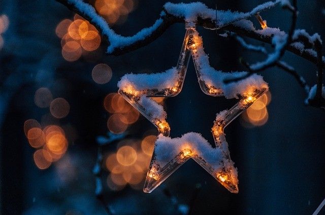 Ein sternförmiges Ornament mit Lichtern hängt an einem verschneiten Ast, beleuchtet vor einem dunklen Hintergrund.