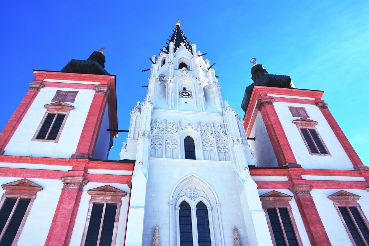 A white church with red accents and intricate Gothic-style carvings. The central tower features a clock and spires.