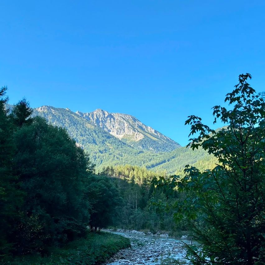 A serene mountain landscape with a clear blue sky, lush greenery, and a winding river flowing through the valley.