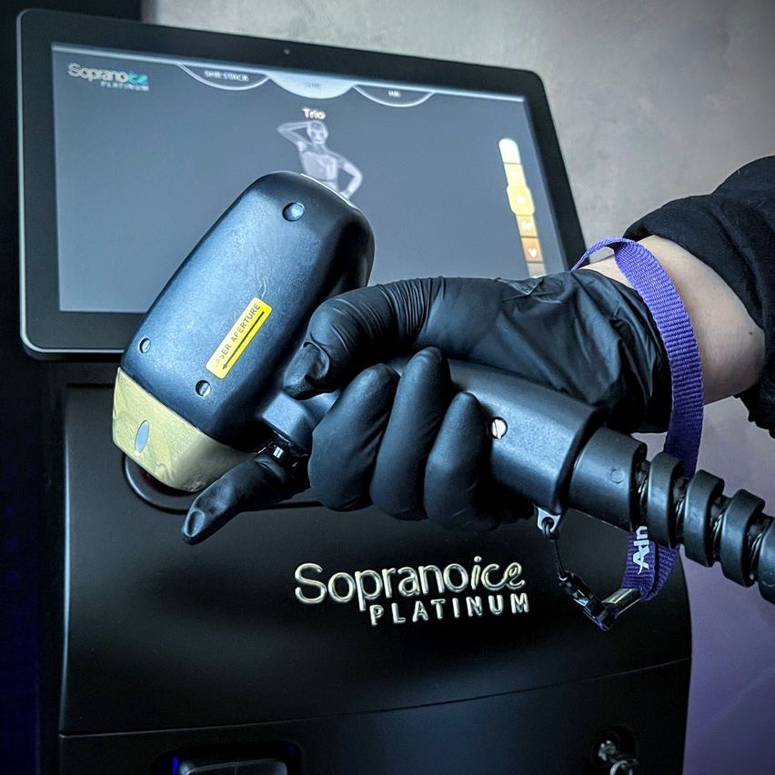 Eine Person in Handschuhen bedient eine Sopranoice Platinum-Maschine und hält ein Handgerät mit einem Monitor, auf dem 'Trio' und andere Optionen angezeigt werden.