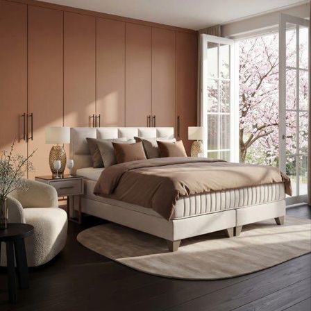 Ein Schlafzimmer mit einem Bett, Kissen und Lampen auf Nachttischen. Es gibt einen Stuhl und einen Tisch mit einer Vase. Der Raum hat einen Holzboden und ein großes Fenster.