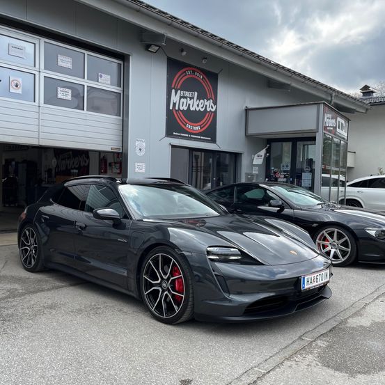 Zwei schwarze Porsche Sportwagen stehen vor einem Gebäude mit der Aufschrift Street Markers. Der nächste Wagen hat ein Nummernschild mit der Aufschrift HAE670 IN.