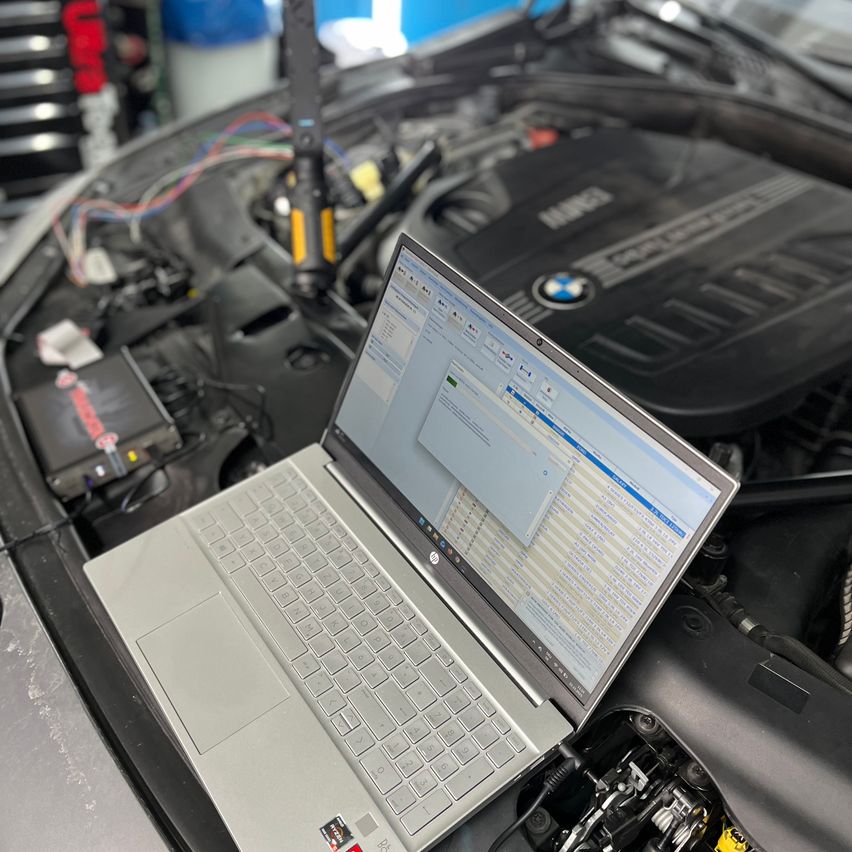 Ein Laptop ist auf einer geöffneten Motorhaube und zeigt eine Diagnoseschnittstelle an. Die Motorhaube ist geöffnet und zeigt den Motor. Ein Diagnosewerkzeug ist an den Laptop angeschlossen.