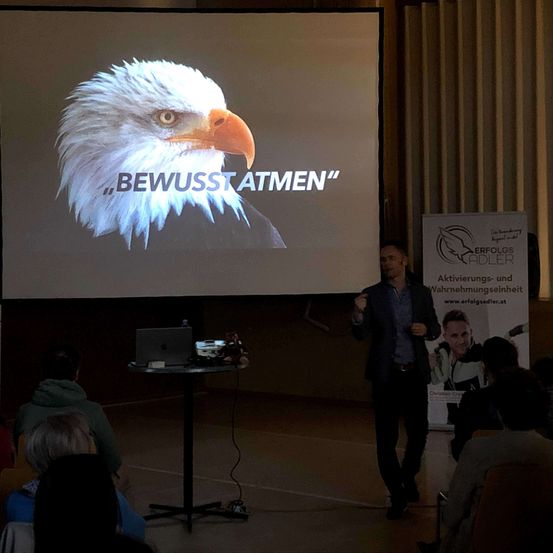 Ein Mann hält eine Präsentation bei einem Seminar mit einem Adlerbild auf der Leinwand, das 'Bewusst Atmen' sagt