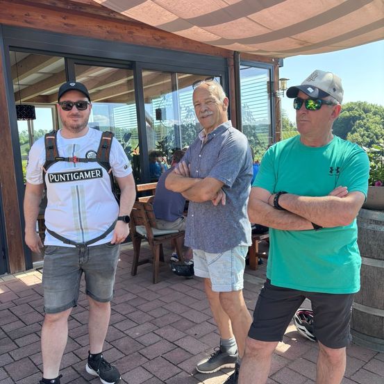 Drei Männer stehen vor einem Gebäude mit einer Ziegelboden, einer mit einem Rucksack und zwei tragen Hüte.