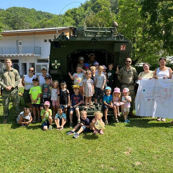 Eine Gruppe von Kindern und Erwachsenen posiert für ein Foto vor einem Militärfahrzeug mit einem Banner.