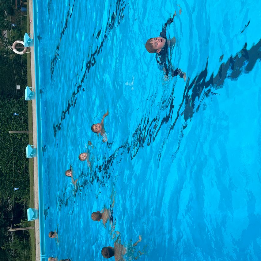 Eine Gruppe von Kindern schwimmt in einem blauen Pool, wobei ein Junge zum Himmel schaut.