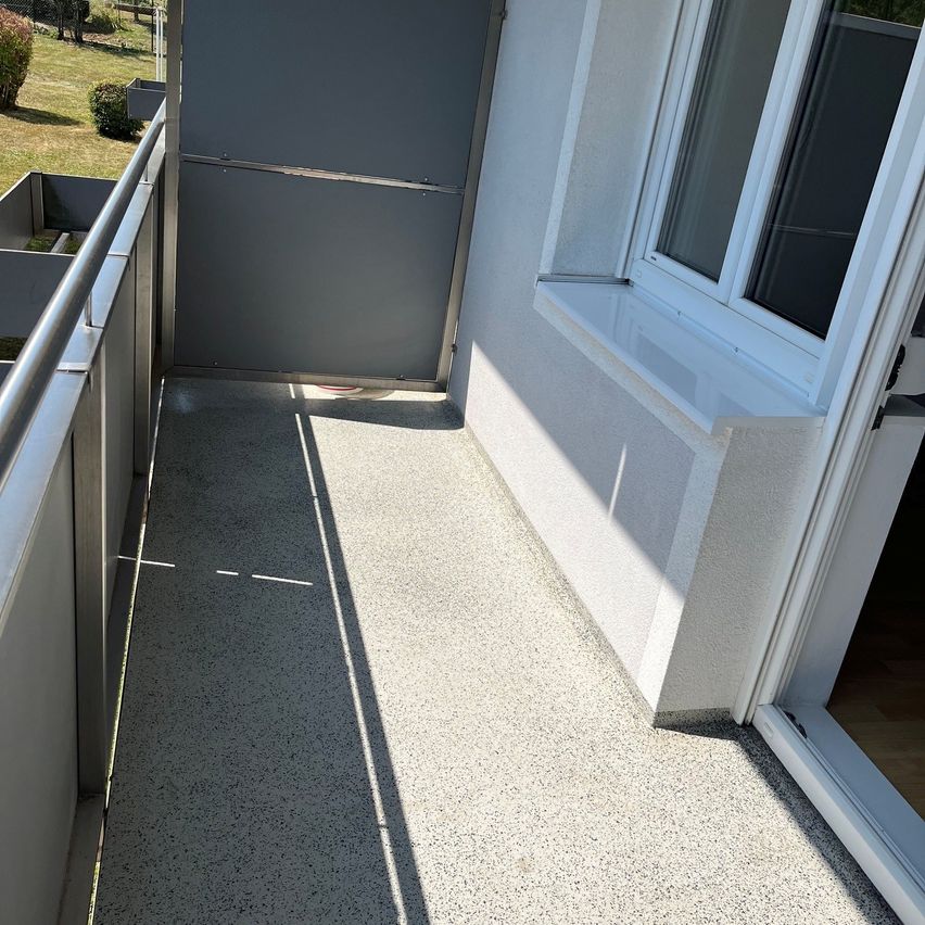 Ein Balkon mit einer geschlossenen Tür und einem Fenster an einem sonnigen Tag. Der Boden besteht aus Beton.