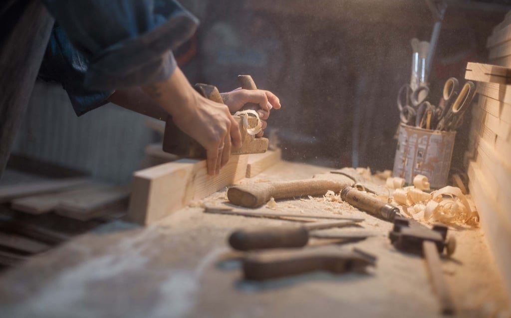 Eine Person schneidet mit einem Meißel einen Holzblock auf einer Werkbank, umgeben von verschiedenen Werkzeugen.
