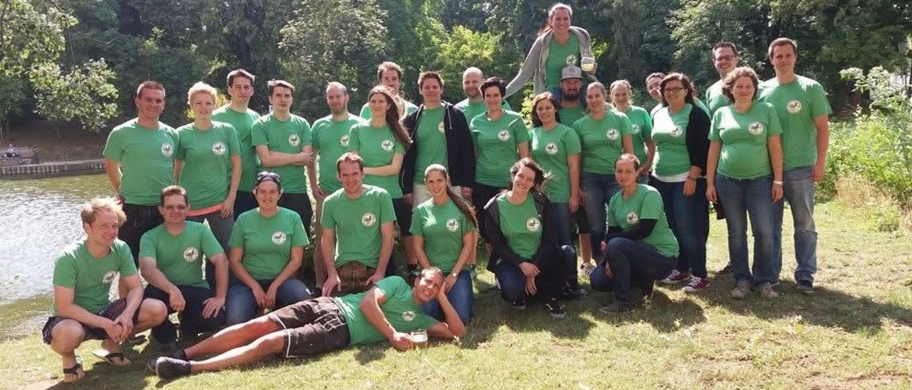 Eine Gruppe von Menschen in grünen T-Shirts posiert für ein Foto in einem Park. Bäume sind im Hintergrund.