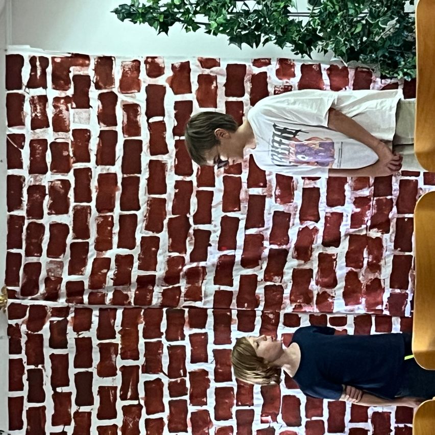 Zwei Jungen stehen vor einer bemalten Ziegelwand, einer schaut nach unten, der andere nach oben.