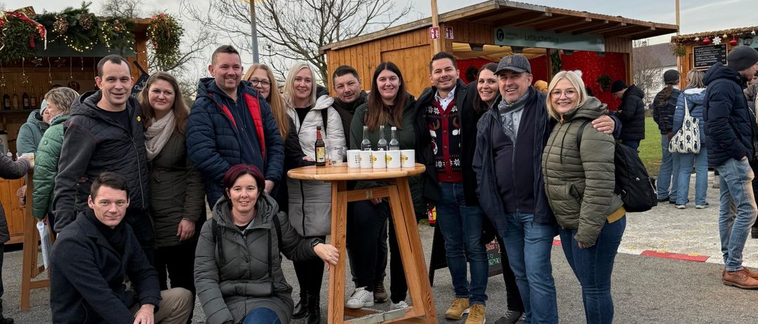 Eine Gruppe von Menschen versammelt sich um einen Tisch mit Flaschen für eine festliche Veranstaltung, lächelt und posiert für ein Foto.