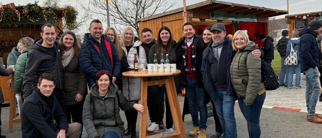 Eine Gruppe von Menschen versammelt sich um einen Tisch mit Flaschen für eine festliche Veranstaltung, lächelt und posiert für ein Foto.