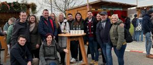 Eine Gruppe von Menschen versammelt sich um einen Tisch mit Flaschen für eine festliche Veranstaltung, lächelt und posiert für ein Foto.