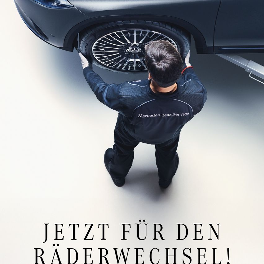 Ein Mann in einer Mercedes-Benz Service-Uniform wechselt einen Autoreifen. Der Reifen ist angehoben und wird vom Mann gehalten. Er trägt weiße Handschuhe. Der Schatten des Autos fällt auf den Boden. Am unteren Rand steht 'Jetzt für den Räderwechsel!'