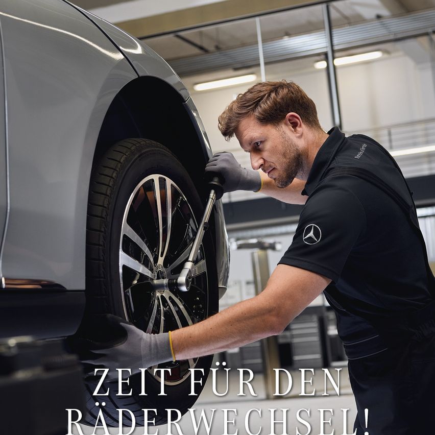 Ein Mann arbeitet in einer Werkstatt an einem Autoreifen. Er trägt Handschuhe und benutzt einen Schraubenschlüssel, um die Radmutter zu festigen. Das Auto ist auf einer Hebebühne gehoben, und der Mann beugt sich über den Reifen. Der Text auf dem Bild lautet 'Zeit für den Raderwechsel!' auf Deutsch.