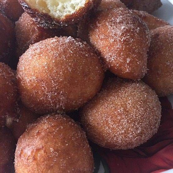 Ein Haufen runder, zuckerbeschichteter Donuts mit einem herausgebissenen Stück. Jeder Donut ist goldbraun, mit Kristallzucker bestreut und liegt auf einem roten Tuch.