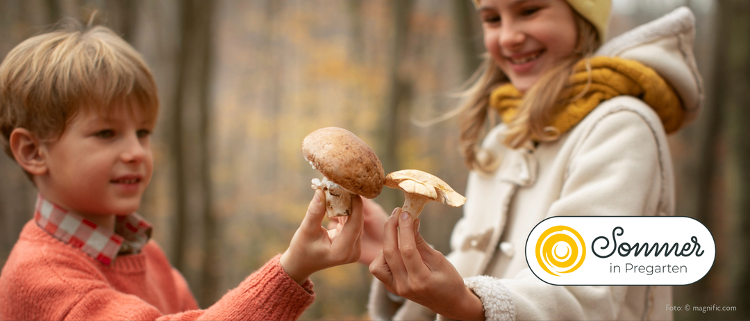 Zwei Personen halten Pilze, wahrscheinlich in einem Wald. Ein Kind auf der linken Seite lächelt und ein Erwachsener auf der rechten Seite lächelt ebenfalls.