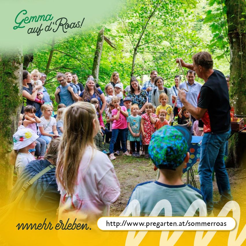 Eine Gruppe von Menschen, einschließlich Kindern, ist in einem Wald für eine Veranstaltung versammelt. Ein erwachsener Mann hält eine Schlange und scheint für die Menge aufzutreten.