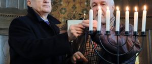 Zwei Männer zünden Kerzen an einer Menora in einer Kirche an. Einer hält eine Kerze, während der andere sie anzündet.